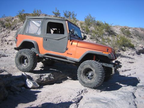 1996 Ford Bronco - An orange Jeep Wrangler TJ navigates a rocky trail under a clear blue sky.