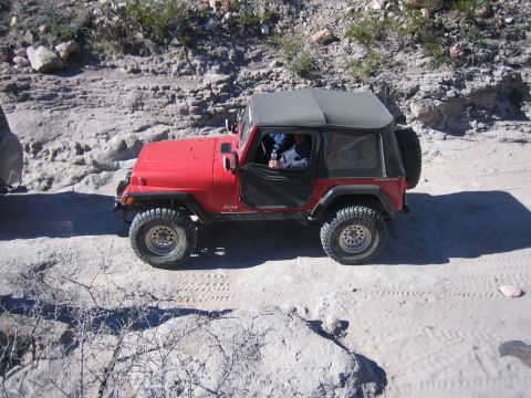 1996 Ford Bronco - A red Jeep Wrangler navigates a rocky, off-road trail under a clear sky.
