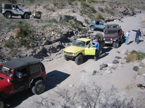 1996 Ford Bronco - A group of off-road vehicles navigate a dusty, rocky trail in a desert landscape.