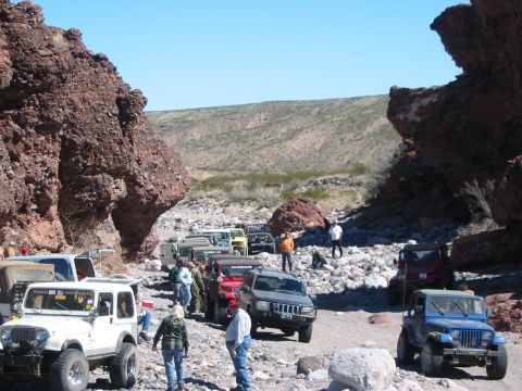 1996 Ford Bronco - A convoy of off-road vehicles navigates a rocky canyon under a clear blue sky.