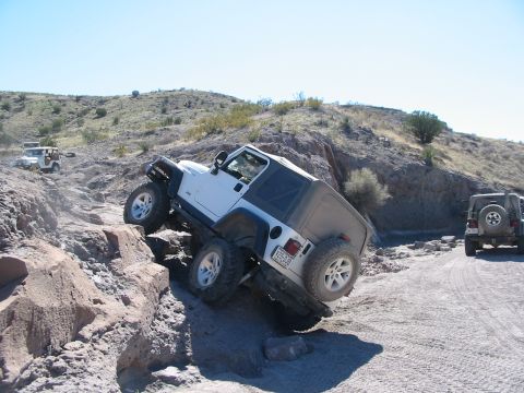 1996 Ford Bronco - Two Jeeps navigating a challenging off-road course with rocky inclines and clear skies.