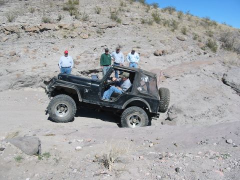1996 Ford Bronco - A black Jeep Wrangler navigates a challenging off-road trail with onlookers present.