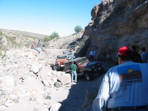 1996 Ford Bronco - A group of Jeeps navigates a challenging off-road trail through a rocky canyon under a clear blue sky.