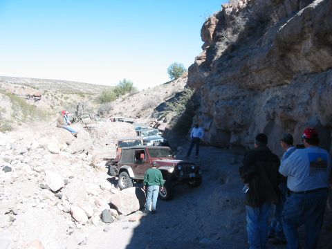 1996 Ford Bronco - A convoy of Jeeps navigates a narrow, rocky canyon trail under a clear blue sky.