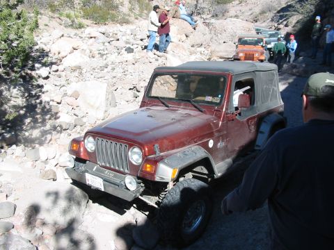 1996 Ford Bronco - A red Jeep Wrangler TJ navigates a rocky trail with other vehicles and people present.