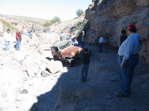 1996 Ford Bronco - A group of people observe a Jeep Wrangler navigating a difficult, rocky off-road path.