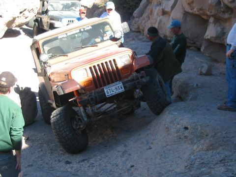 1996 Ford Bronco - A Jeep Wrangler navigates a difficult rocky terrain with other vehicles and people present.