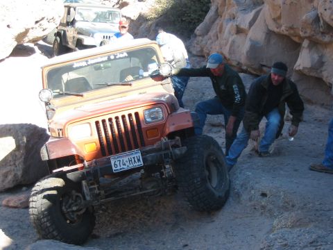 1996 Ford Bronco - An orange Jeep Wrangler with a visible license plate navigates a challenging off-road trail, with another Jeep visible in the background.