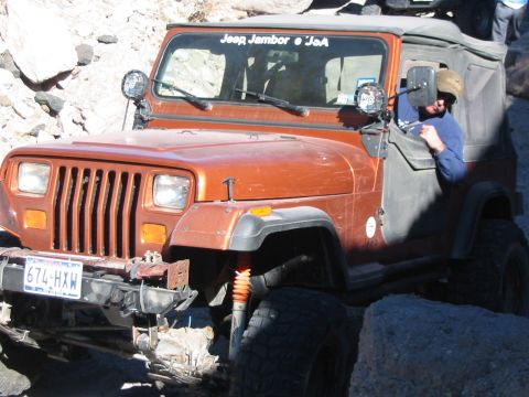 1996 Ford Bronco - Orange Jeep Wrangler navigates rocky terrain with a driver visible inside.