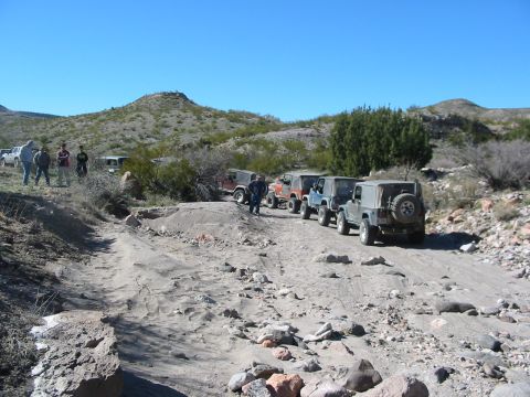 1996 Ford Bronco - A group of Jeeps navigates a rough, off-road path under a clear blue sky.