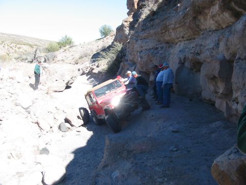 1996 Ford Bronco - A red Jeep Wrangler navigates a narrow, rocky off-road path with several onlookers.