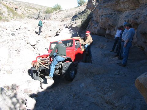 1996 Ford Bronco - A red Jeep Wrangler maneuvers through a challenging rocky path, observed by several onlookers.