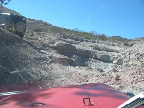 1996 Ford Bronco - Two off-road vehicles navigate a steep, rocky trail under a clear blue sky.