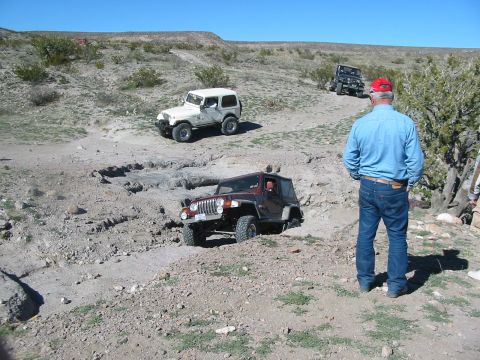 1996 Ford Bronco - Multiple Jeep Wranglers traverse a challenging off-road trail under a clear blue sky.