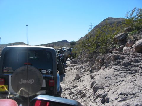 1996 Ford Bronco - A line of Jeep Wranglers navigates a rocky off-road trail under a clear blue sky.