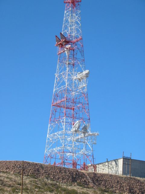 1996 Ford Bronco - A tall radio tower stands against a bright blue sky, with a building visible near its foundation.