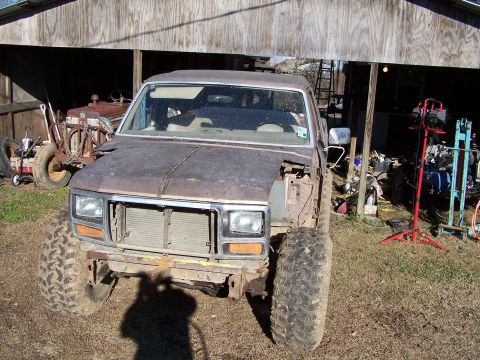 1981 Ford Bronco - This weathered pickup truck sits outside a barn, showing signs of age and modification with its oversized tires.