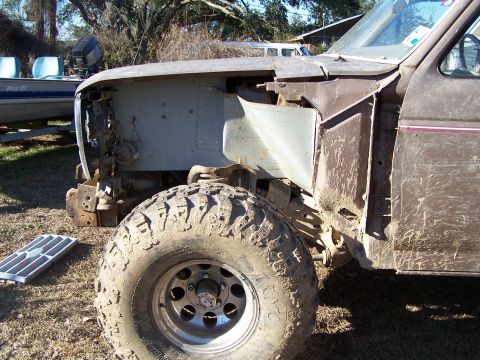 1981 Ford Bronco - The front fender and wheel of a brown truck are visible, with the headlight area disassembled.