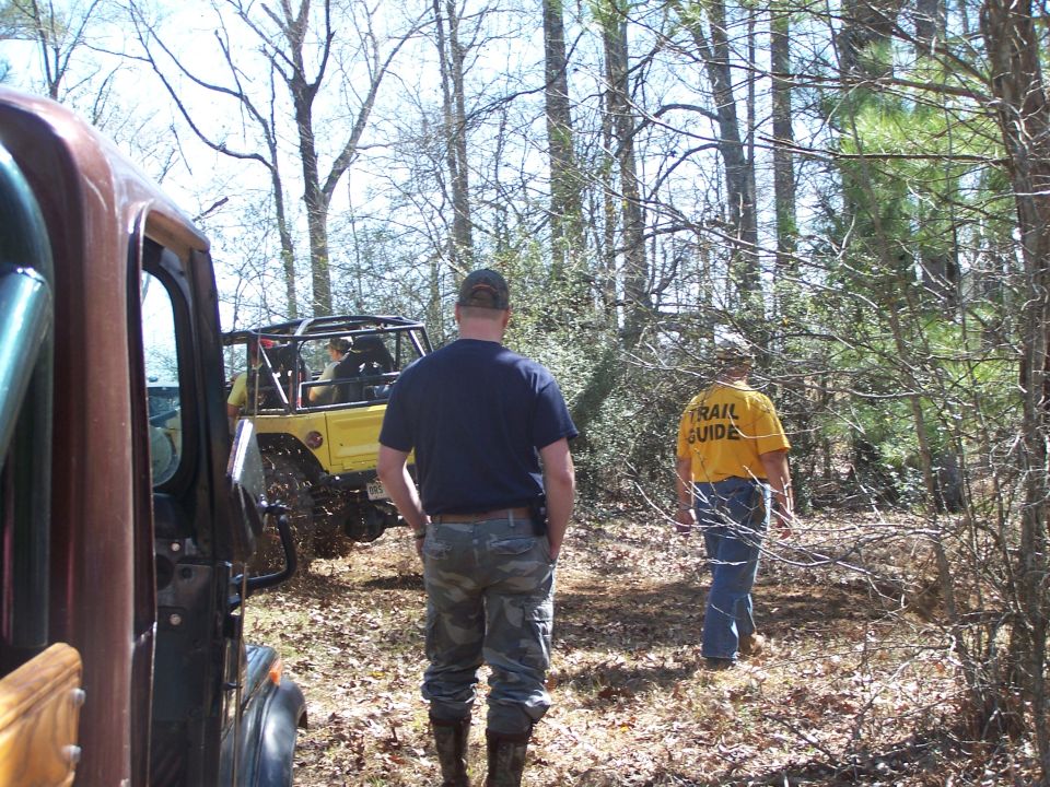 Yellow off-road vehicle with roll cage in woods; trail guide shirt visible