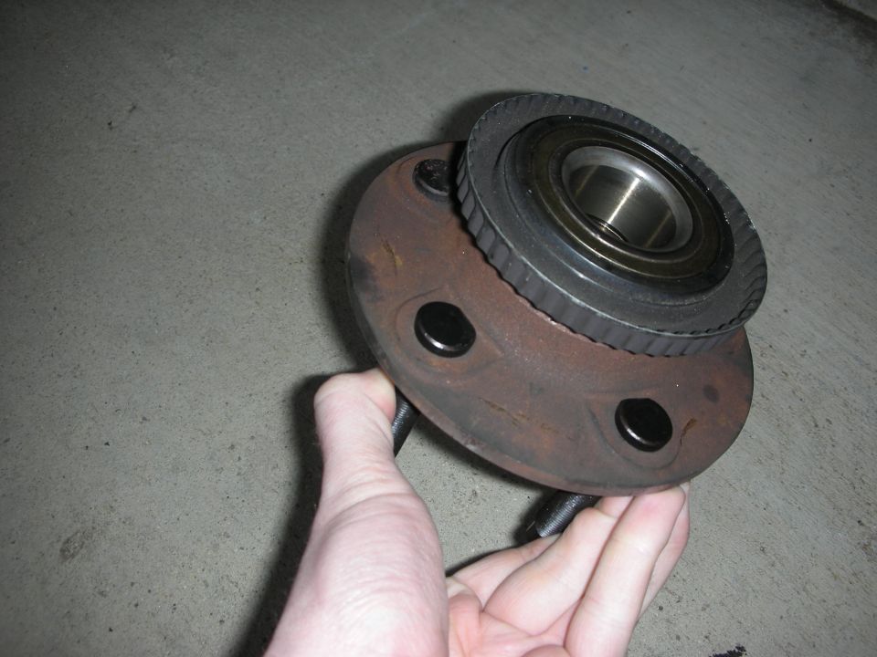 Hand holding a rusty wheel hub assembly with two bolt holes