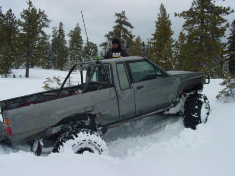 1986 Ford Bronco - A pickup truck is partially buried in snow, with trees visible in the winter landscape.