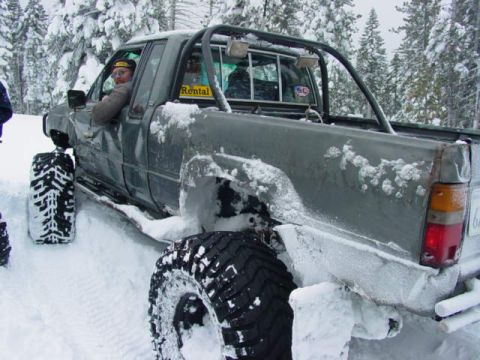 1986 Ford Bronco - Off-road pickup truck with oversized tires is stuck in deep snow.