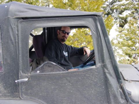 1986 Ford Bronco - A man is seated inside a vehicle with a soft top, surrounded by a snowy, wooded environment.