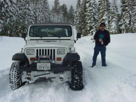 1986 Ford Bronco - A man stands beside a white Jeep Wrangler partially buried in snow, surrounded by snow-covered trees.