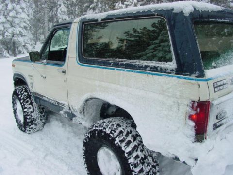 1986 Ford Bronco - A 1986 Ford Bronco navigates a snowy landscape, its large tires kicking up snow.