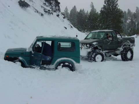 1986 Ford Bronco - Two off-road vehicles are stuck in deep snow on a mountain pass.