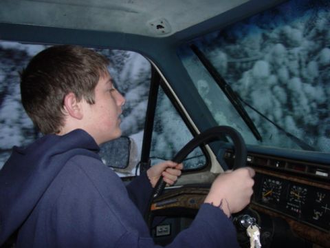 1986 Ford Bronco - A young person drives through a snowy landscape, the interior of the vehicle visible.