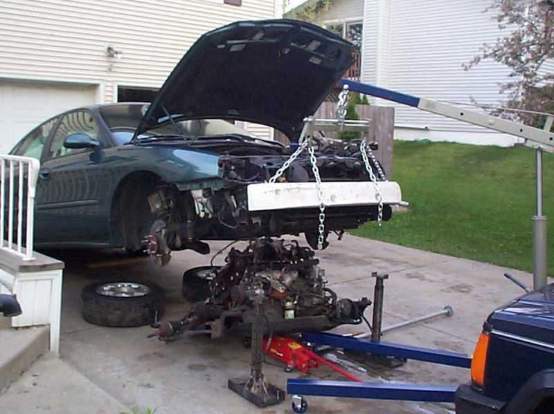 Engine hoist pulling engine and transaxle from a teal Ford Taurus in a driveway