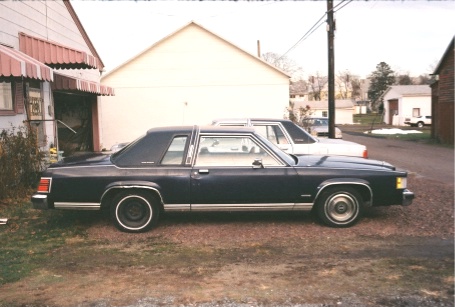 1984 Mercury Grand Marquis - Two sedans are parked in a driveway next to a house and garage.