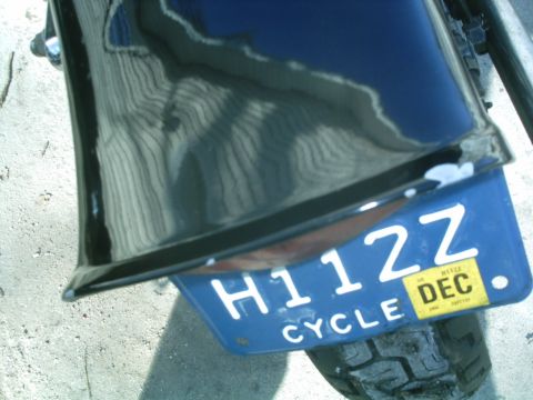1979 Ford Bronco - Rear view of a motorcycle fender with a blue license plate reading H112Z and a yellow DEC sticker.