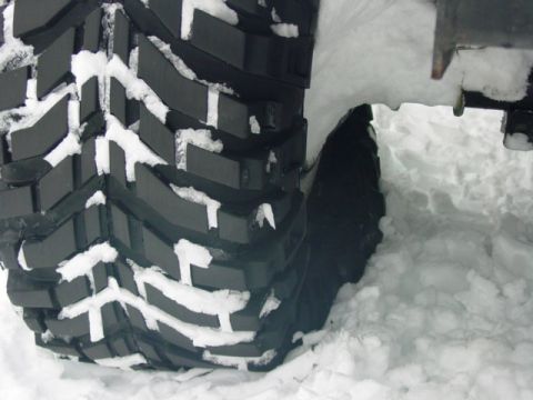 1986 Ford Bronco - A close-up view of a large tire, its aggressive tread pattern packed with snow.