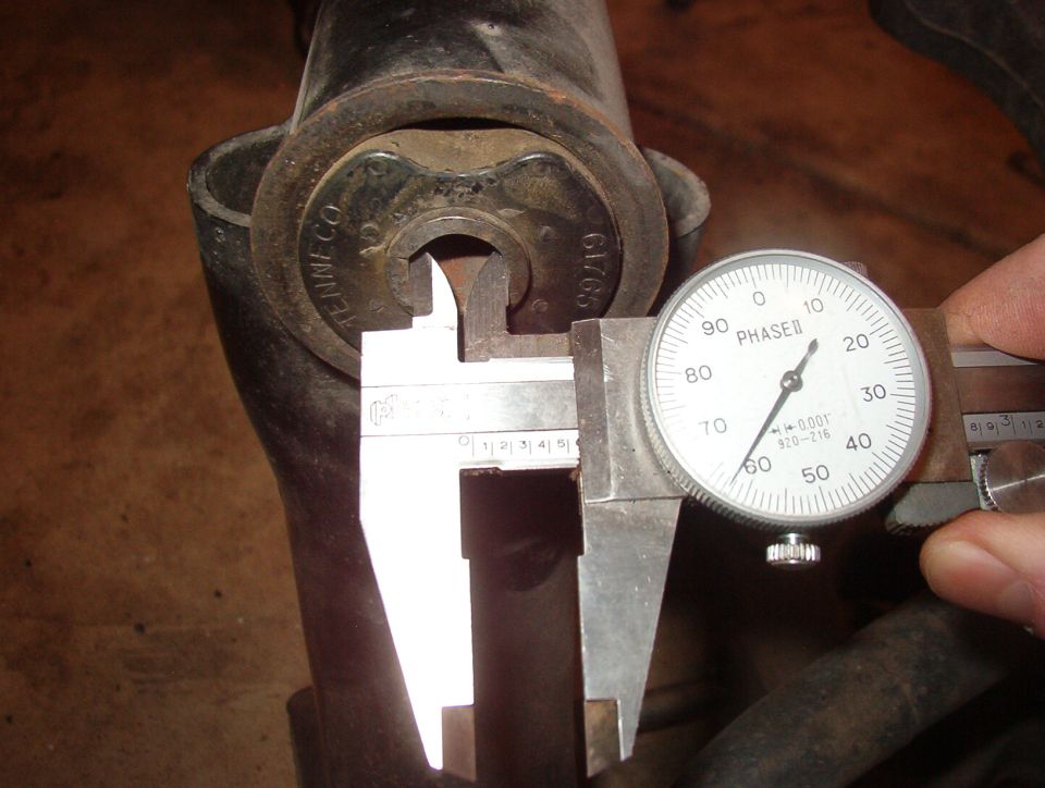 Dial calipers measuring a metal component with 'TENNECO' and '61/65' visible