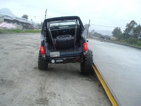 1989 Ford Bronco - Rear view of a 1989 Ford Bronco modified with a roll cage and spare tire in the bed.