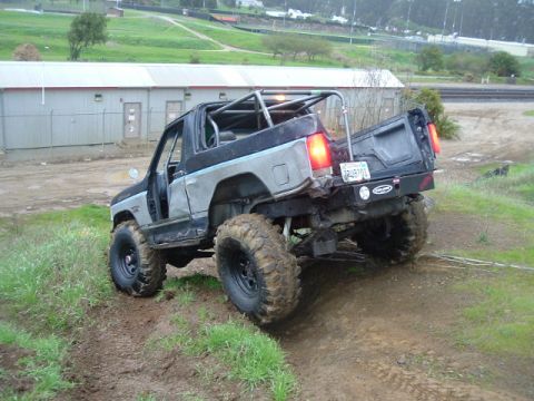 1989 Ford Bronco - Modified 1989 Ford Bronco tackling an off-road trail with large tires and a custom roll cage.