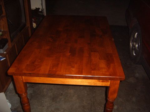 1988 Ford Bronco - A wooden dining table is shown in a garage, with a car wheel partially visible on the right side.