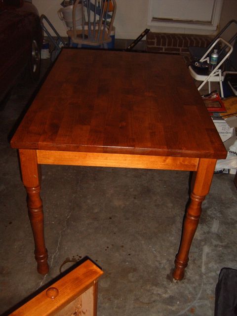 1988 Ford Bronco - A wooden dining table with a dark finish sits on a concrete floor, with various items in the background.