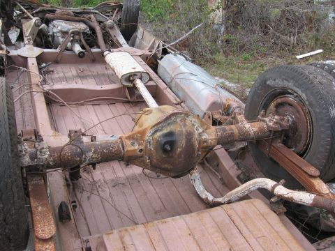 1974 Ford F-100 - The undercarriage of a heavily rusted truck, showing the rear axle, exhaust system, and fuel tank.