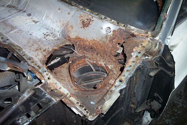 Heavily rusted metal cowl area with large holes, showing internal components and a circular vent