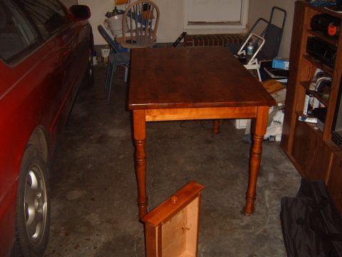1988 Ford Bronco - A red car is parked in a garage next to a wooden dining table.