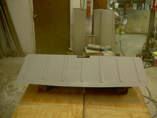 Gray tailgate with raised vertical ribs, resting on wooden supports in a workshop