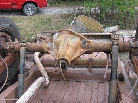 1974 Ford F-100 - A rusty rear axle assembly is visible in the bed of a truck, with a red pickup truck in the background.