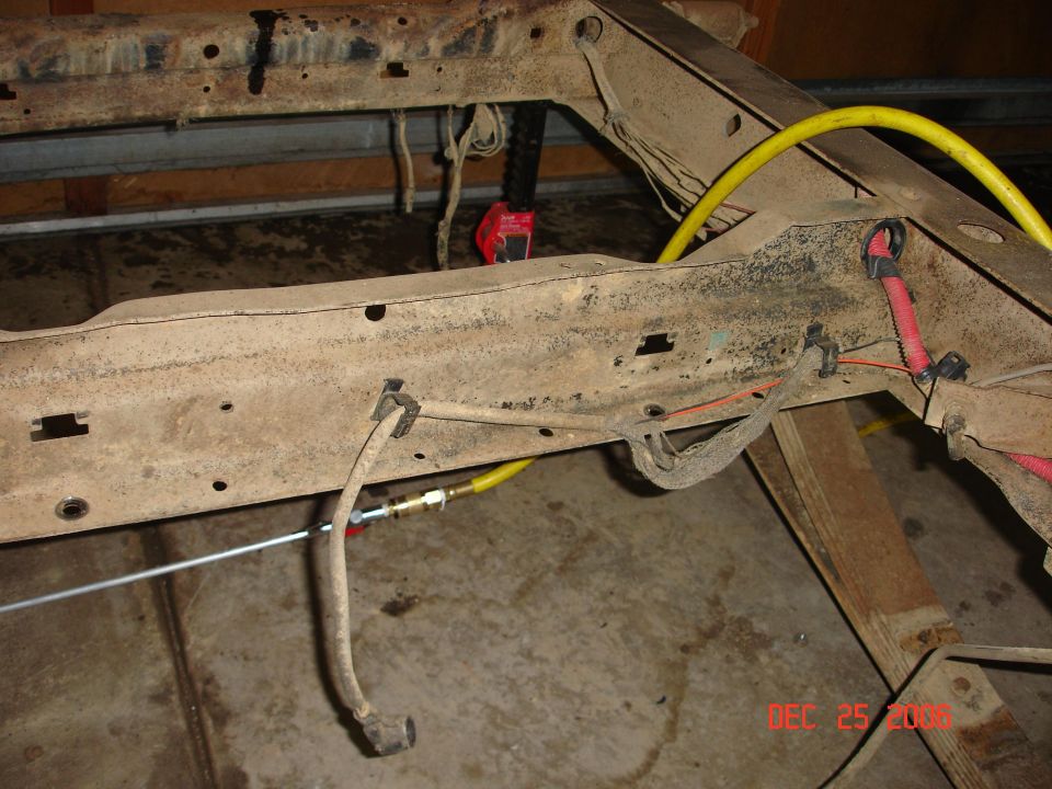 Rusty vehicle frame with yellow hose and red wiring, showing brake lines and suspension components