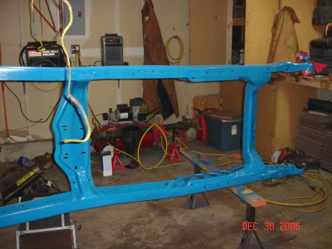 1978 Ford Bronco - A bright blue painted vehicle frame is shown on jack stands, with various tools and equipment visible in the garage setting.