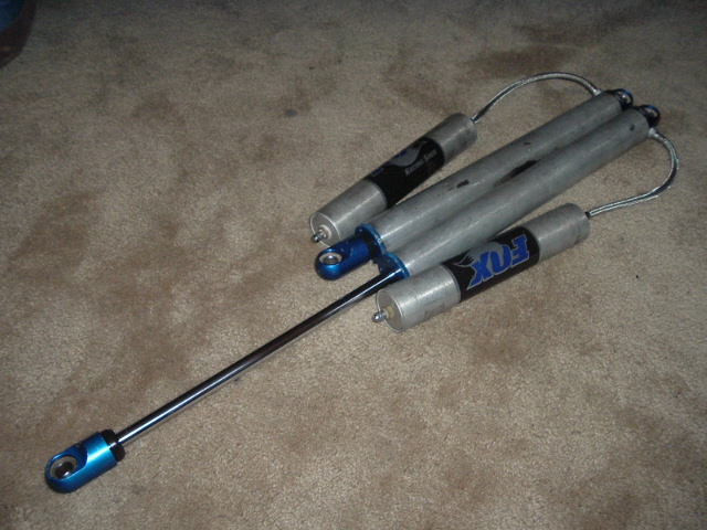 Pair of Fox remote-reservoir shocks with blue anodized eyelets on carpet