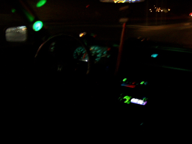 Car interior at night, dashboard lights and radio display illuminated, green lights on ceiling