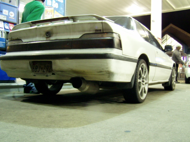White coupe with a spoiler and aftermarket exhaust, viewed from the rear